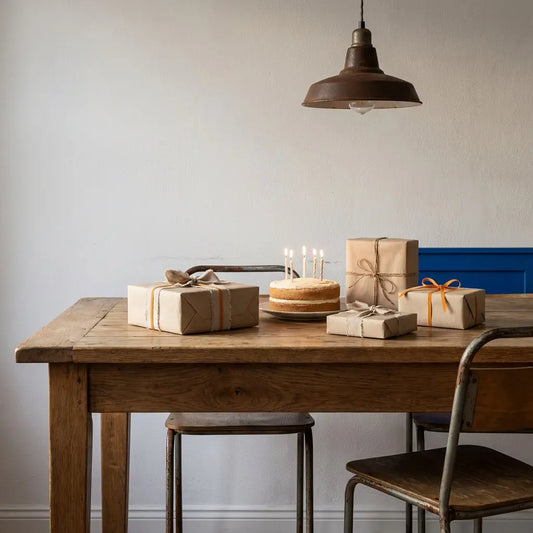 Gemütliches Esszimmer mit Esstisch, verstreuten Geschenkboxen und Vanillekuchen mit Kerzen; intime, minimalistische 15. Geburtstag-Szene, warmes Licht