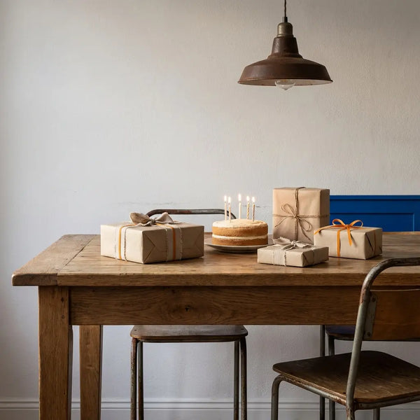 Gemütliches Esszimmer mit Esstisch, verstreuten Geschenkboxen und Vanillekuchen mit Kerzen; intime, minimalistische 15. Geburtstag-Szene, warmes Licht