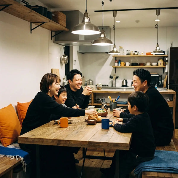 Kleine Familie und enge Freunde versammeln sich um einen Holztisch, teilen Lachen und Geschenke – abschlussgeschenk ideen in hellem, minimalem Raum mit Holz und Metall