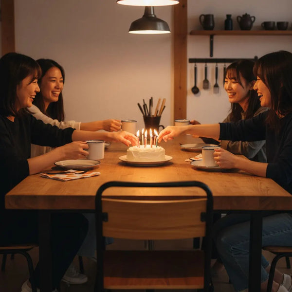 Gemütliche Küche mit Freunden um Holztisch, Hände greifen nach Kuchen und Tassen – coole Geburtstagsgrüße in minimalistischer Industrieästhetik