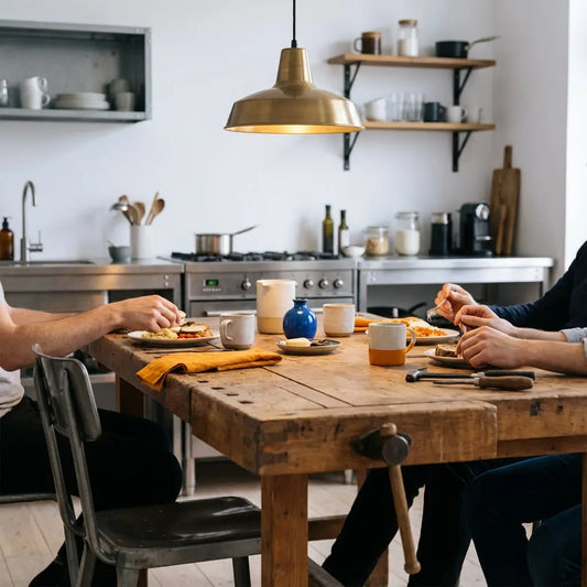 Kleine Familie beim gemeinsamen Essen an einem Holztisch in warmer, minimalistischer Wohnküche, Fokus auf Zusammenhalt — Danksagung Hebamme