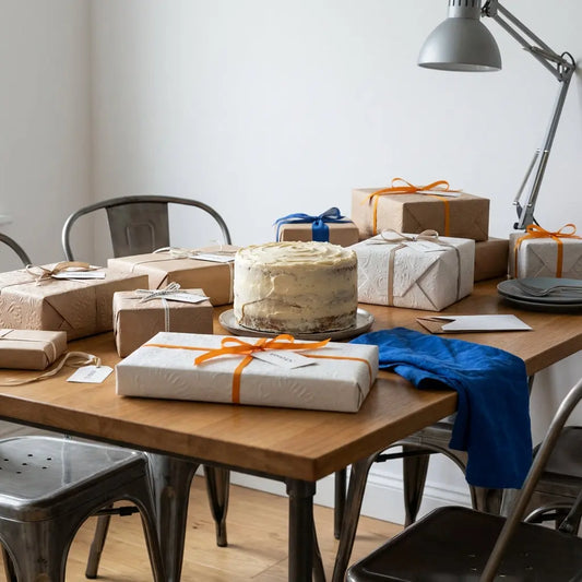Gedeckter Esstisch mit sorgfältig verpackten Geschenken und einfachem Vanillekuchen, warme Holzoberfläche und dezente Metalldetails im industriellen Stil – erwachsenen Sohn