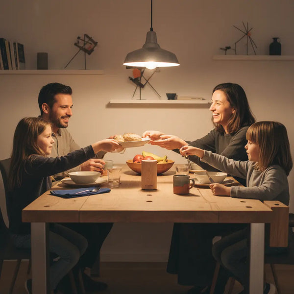 Intime Abendsszene mit Familie an einem aufgeräumten Holztisch und dem Produkt aus Referenzfotos im Zentrum – warme Stimmung, Geschenke für Schwangere