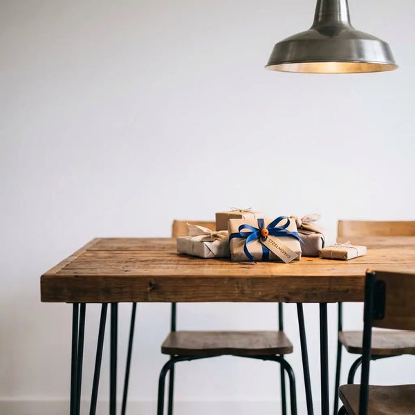 Rustikal-moderner Esstisch mit dezent verpackten Geschenken und graviertem Metallanhänger, warme Holzoberfläche, leichte Metalldetails, Fokus auf Materialität, geschenke für trauzeugen