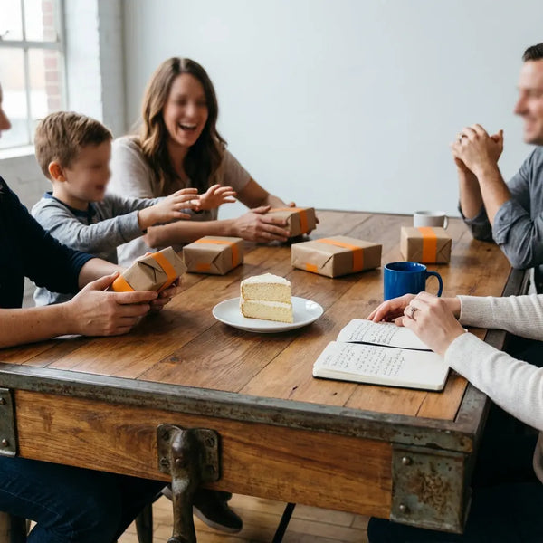 Kleine Gruppe um Tisch mit verpackten Geschenken, Vanillekuchen und Notizbuch – warmes, industrielles Motiv für geschenke für menschen die alles haben in minimalistischem Stil