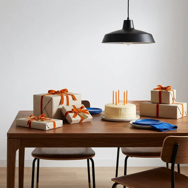 Intimes Esszimmer mit Holztisch, mehreren sorgfältigen Geschenken und einfachem Vanillekuchen — geschenke zum 70. geburtstag, warme Beleuchtung und metallische Akzente
