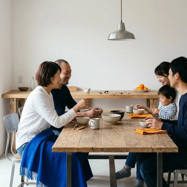 Kleine Familie am Holztisch, warme Beleuchtung, Hände teilen Geschirr und lachen gemeinsam – ideal für geschenkideen babyparty