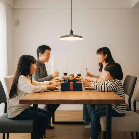 Kleine Familie am hellen Holztisch, Hände greifen nach Tellern und einem Geschenk in warmer, leicht industrieller Stimmung – geschenkideen für seniorinnen