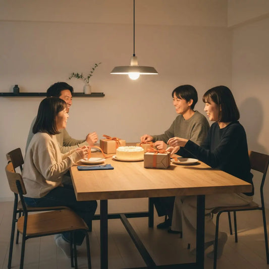 Kleine Familie feiert im warmen Esszimmer mit Holz- und Metalldetails um einen Tisch mit Geschenkboxen und Vanillekuchen – geschenkideen für 18-jährige jungs