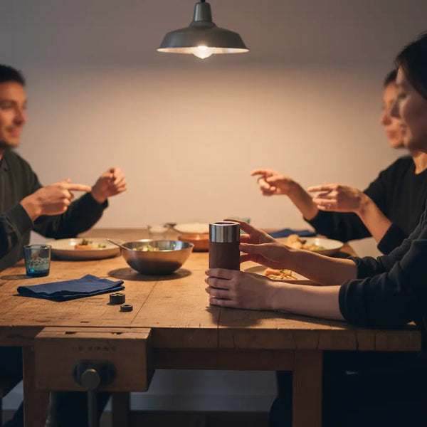Intimes Abendmotiv am Holztisch mit Händen, Metallakzenten und dem Produkt aus den Referenzfotos – geschenkideen für eltern; warme Beleuchtung, industrielle Ästhetik, keine klar erkennbaren Gesichter.