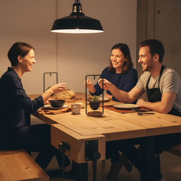 last minute geschenke mama: intime Abend‑Szene mit Familie am Holztisch, warme Beleuchtung, industrielle Metallakzente, Hände greifen, Produkt aus den Referenzfotos sichtbar.