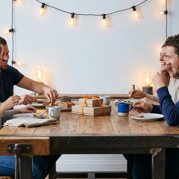 Warm beleuchteter Esstisch mit Holzoberfläche, Metallakzenten und Geschenkpaketen – Paket als Geschenk verschicken in einer intimen, einladenden Szene.