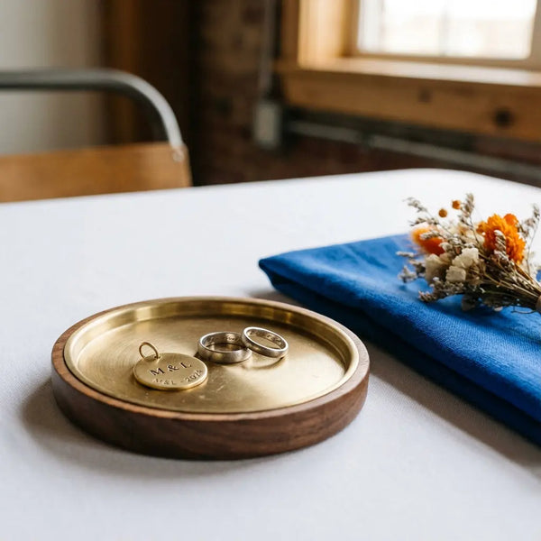 Was kann man zur standesamtlichen Hochzeit machen? Minimalistische Tischszene mit Ringen auf Holz Metallteller, graviertem Metallanhänger als Gastgeschenk, Leinenserviette und Trockenblumen, warmes Licht
