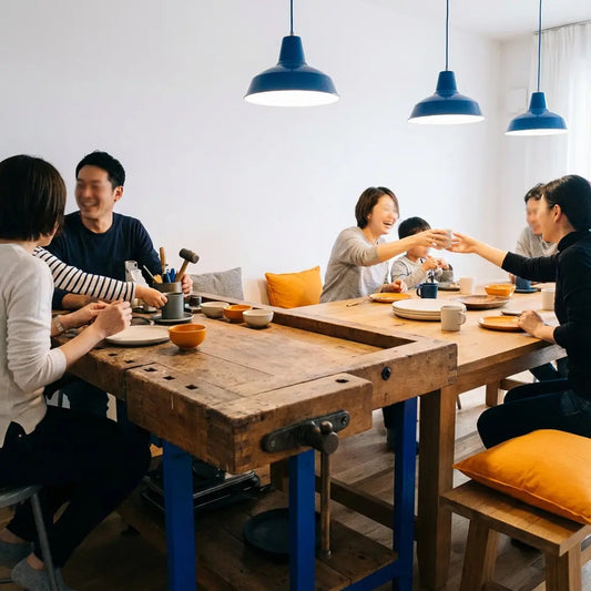 Was schenkt die Schwiegermutter der Braut? Kleine Familie um Esstisch mit Holzoberfläche und Metalldetails, warme Beleuchtung, Hände greifen nach Tellern, minimalistisch und authentisch.