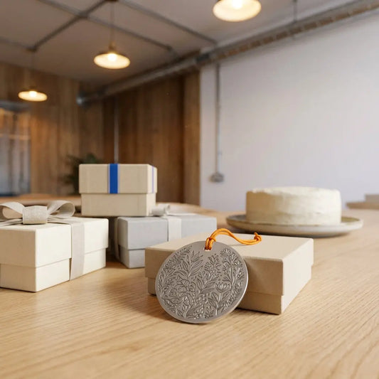Nahaufnahme Holztisch mit Geschenkboxen, graviertem Metallanhänger und Vanilletorte im Hintergrund in minimalistischem Industrieambiente, was schenkt man zur bestandenen pruefung