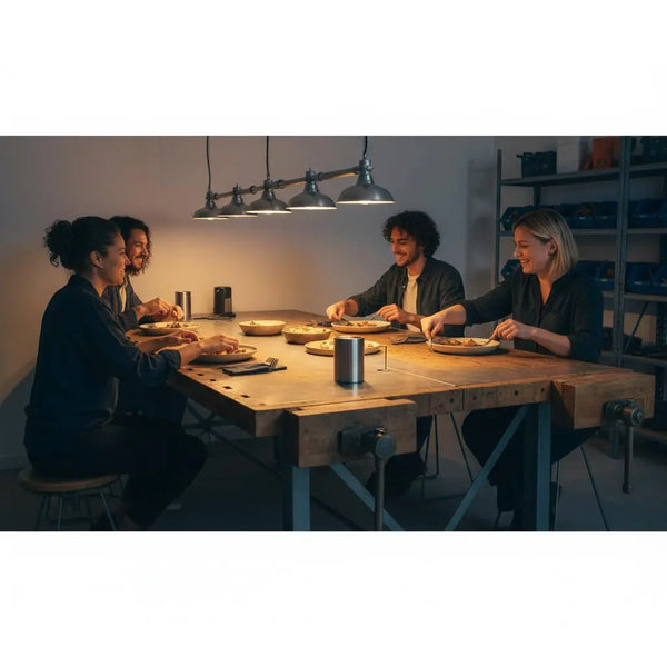 Was sollte man bei einer Hochzeit schenken? Intime, abendliche Szene mit Freunden um einen Esstisch, Hände greifen nach Tellern, dezenter Industrie-Charme mit Holz und Metall.