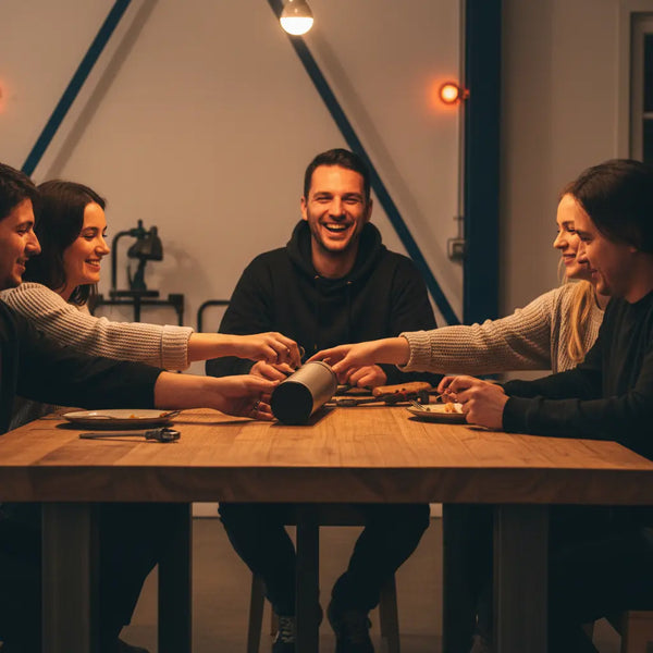 Abendliche Werkstattszene mit Freunden am Holztisch, warme Beleuchtung, dezente Metallakzente und Hände bei der Arbeit – Wichtel-Produkt präsent auf der Werkbank, intime Atmosphäre.
