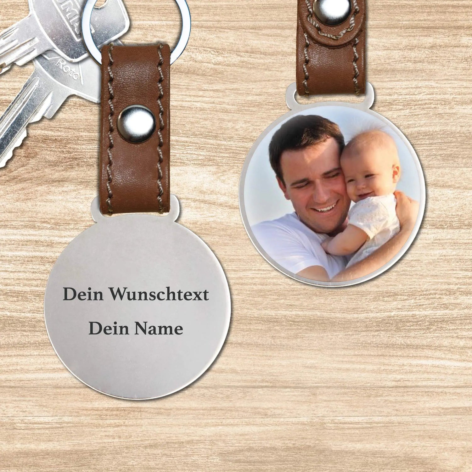 Zwei runde Fotoanhänger aus Stahl an braunen Lederbändern auf Holz: einer mit Foto von Vater und Baby, einer mit graviertem Wunschtext