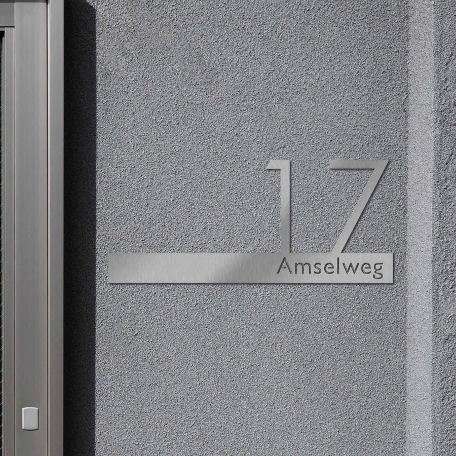 Hausnummer mit Namen in Edelstahl an grauer Fassade